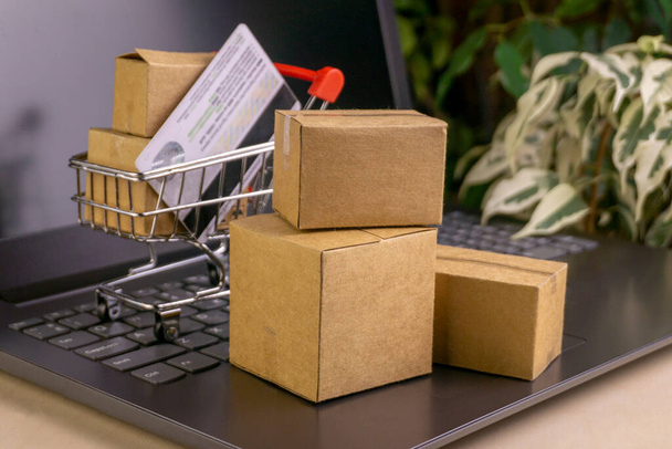 online shopping concept. little shopping cart, boxes, colorful bags, bank card, dollars stand on laptop - Foto, Imagen