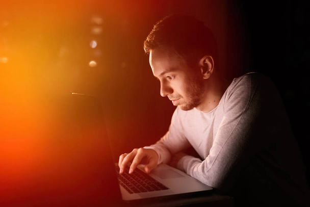  mies istuu työpöydän ääressä ja selailee kannettavaa tietokonetta kotona, keskittyy työhön - Valokuva, kuva