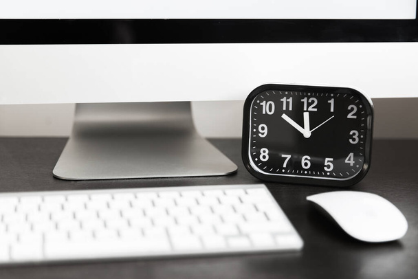 Computer with white keyboard and black clock on wooden table. Template - 写真・画像