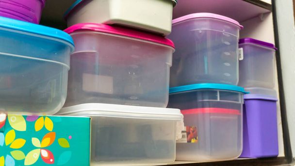 キッチンキャビネットにきれいに配置された食品保管用プラスチック容器の山。木の棚の上のカラフルな食品容器. - 写真・画像