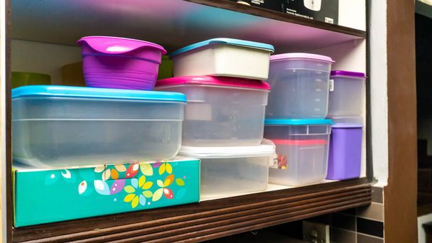 Hromádky plastové nádoby pro skladování potravin úhledně rozmístěné na kuchyňské skříni. Barevná nádoba na jídlo na dřevěné polici. - Fotografie, Obrázek