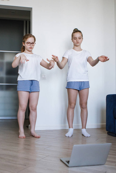 10代の少女2人がノートパソコンのモニターの前で踊りを学ぶ。コロナウイルス隔離家庭教育。ホームアイドル。選択的フォーカス。ぼかしの背景. - 写真・画像
