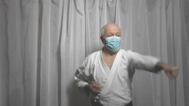 In white karategi and medical mask, an adult athlete is training blows and blocks with his hands - Séquence, vidéo