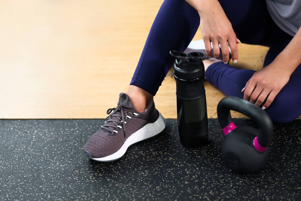 The concept of the gym sport. Fitness equipment. A woman sits on the floor in sneakers. A kettlebell and dumbbells. - Φωτογραφία, εικόνα