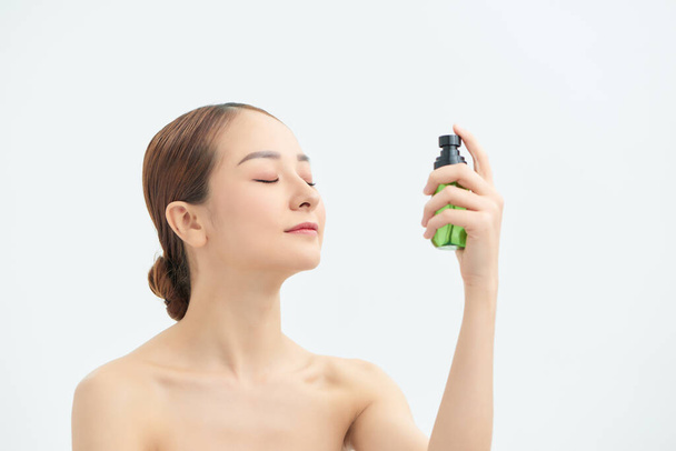 Mujer joven aplicando agua termal en la cara sobre fondo blanco. Producto cosmético
 - Foto, Imagen