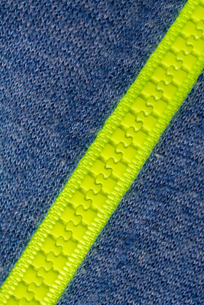 Detailní záběr jasně zeleného zipu uzavřeného uprostřed modrého vzoru tkaniny, pohybující se diagonálně zprava shora dolů vlevo - Fotografie, Obrázek