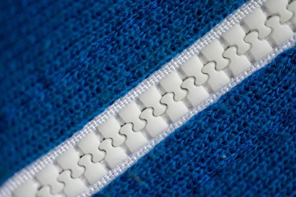 Detailní záběr bílého plastového zipu uzavřeného uprostřed struktury modré tkaniny, zdola vlevo nahoře vpravo - Fotografie, Obrázek