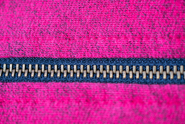 Close-up de um zíper de cobre atravessando da esquerda para a direita no meio sobre uma textura de tecido magenta e preto
 - Foto, Imagem