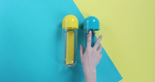 blue and yellow bottles lie on a blue and yellow background, and a female hand takes one bottle - Felvétel, videó