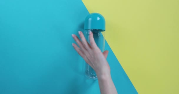 blue and yellow bottles lie on a blue and yellow background, and a female hand takes one bottle - Кадры, видео