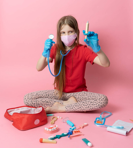 Personal protective equipment: a teenager girl in a medical mask and blue gloves plays a nurse and holds a stethoscope. - Foto, immagini