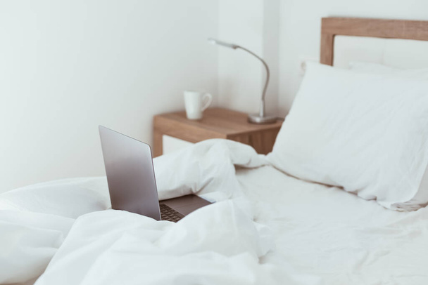 Az otthoni karantén önzárás koncepciója. Laptop a be nem vetett ágyban. Kényelmes és kényelmes távoli otthoni iroda. Modern apartmanok napfénnyel és minimalista kialakítással. Vigyázz magadra a járványban.. - Fotó, kép