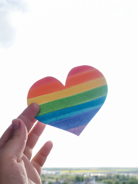 Rainbow Heart, концепция прав lgbt, рука держит сердце, окрашенное как флаг ЛГБТ, силуэт против солнца. - Фото, изображение