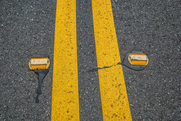 Uma linha amarela dupla na rua com refletores de pista em ambos os lados para ver à noite para ficar na pista
 - Foto, Imagem