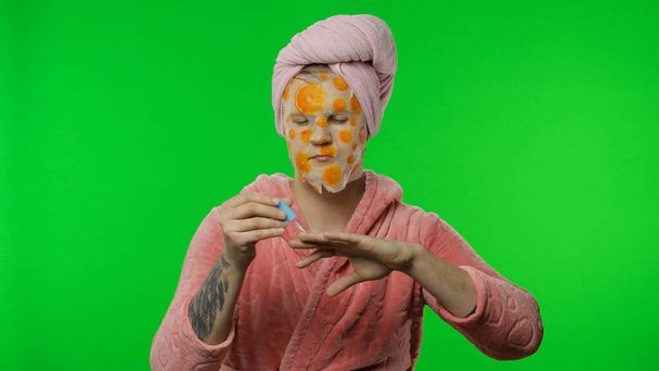 Homme transsexuel en peignoir avec masque facial peignant ses ongles de main. Clé chromatique
 - Photo, image