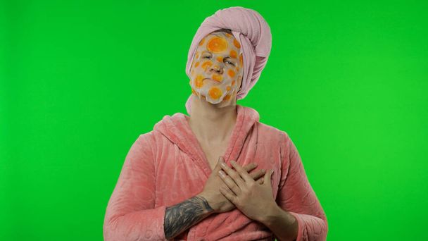 Transsexueller Mann im Bademantel mit Gesichtsmaske und Liebesherz-Zeichen. Chroma-Schlüssel - Foto, Bild