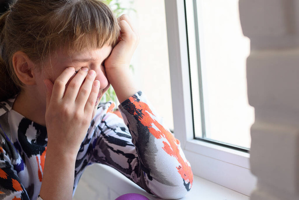 Loukkaantunut tyttö itkee katkerasti ikkunassa
 - Valokuva, kuva