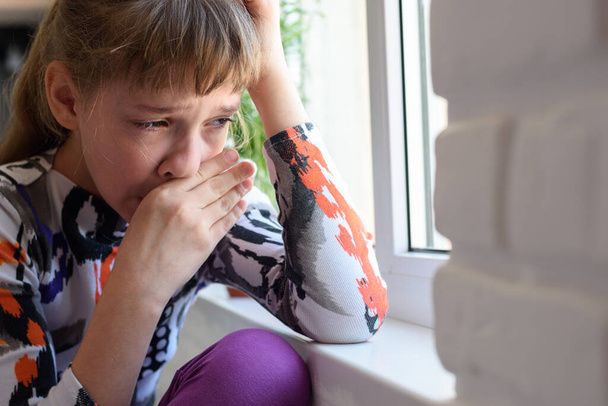 Dívka hořce pláče na okno utírá si slzy rukou - Fotografie, Obrázek
