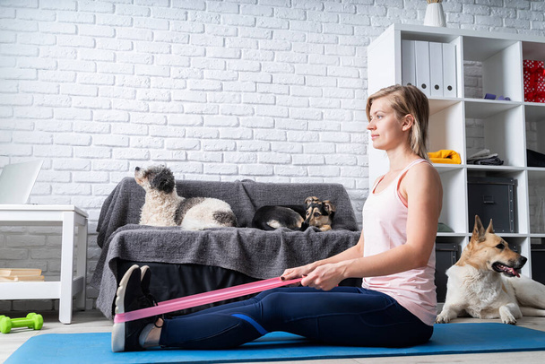 Quédate en casa. Fitness en casa. Mujer haciendo ejercicio con goma banda de resistencia en casa
 - Foto, Imagen