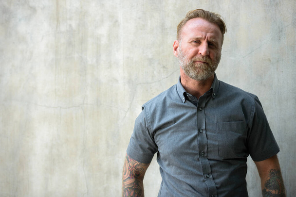 Portré érett jóképű szakállas férfi kézzel tetovált ellen beton fal szabadban - Fotó, kép