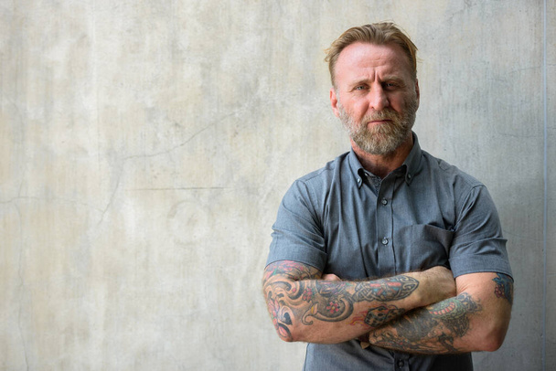 Portré érett jóképű szakállas férfi kézzel tetovált ellen beton fal szabadban - Fotó, kép