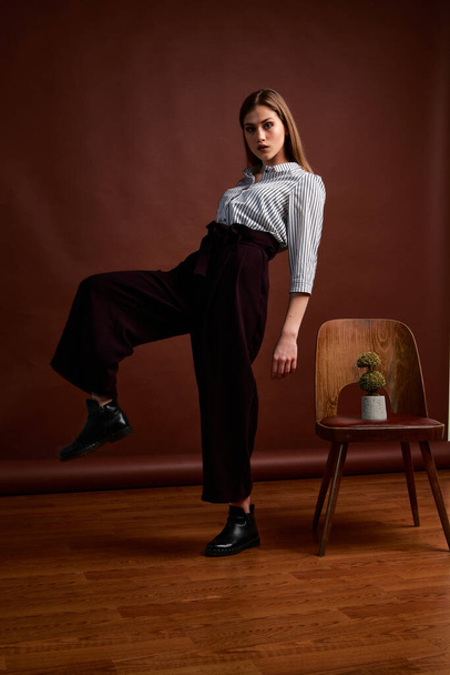 Mininalism style classic studio photo set of the young independent woman. Gorgeous young female in classic suit, black shoes and grey coat. Vintage chair. Woman's clothes. Fashionable clothes. - Foto, imagen