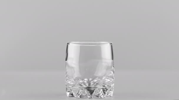 薄い灰色の背景に隔離されたガラスの近くに注ぐミルク - 映像、動画