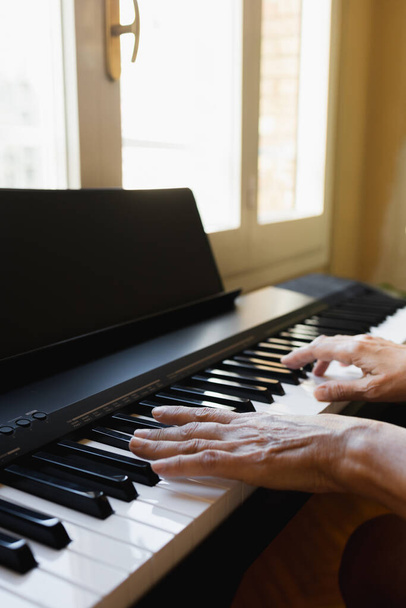 Manos de una anciana tocando el piano en una casa frente a una ventana
 - Foto, imagen
