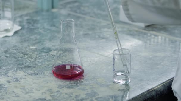 Bediener nimmt eine Probe von Wasser oder Lösung in einem Messrohr vor einem Chemieindikatorkolben aus nächster Nähe - Filmmaterial, Video