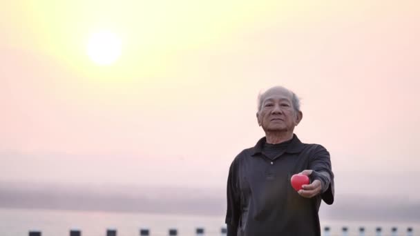 Man senior met rood hart en vrolijke glimlach in de ochtend met de zonsopgang achter de rug. Gezondheidszorg, Gezond met lichaamsbeweging en een gezonde start, verzekering, wereldhartdag, Medische verzekering.  - Video