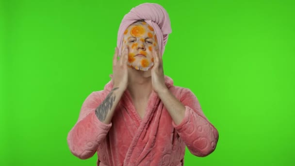 Portrait of transsexual man in bathrobe looking in mirror wearing face mask - Footage, Video