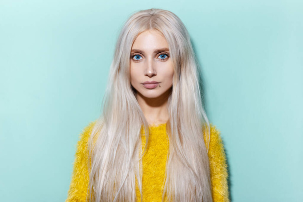 Studio portrait of beautiful blonde girl with blue eyes wearing yellow sweater on cyan, aqua menthe color. - Photo, Image