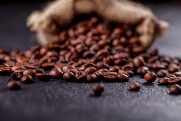Roasted, aromatic coffee beans sprinkled from a canvas bag on a dark surface. The concept of the tradition of morning coffee. Side upper view - Fotoğraf, Görsel