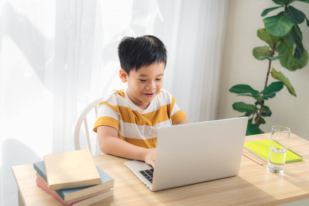 Asien preteen Junge, der online auf Laptop mit lächelndem und lustigem Gesicht zu Hause lernt. Online-Bildung und E-Learning-Konzept. - Foto, Bild