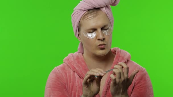 Transsexual man in bathrobe with eye patches making manicure. Chroma key - Footage, Video