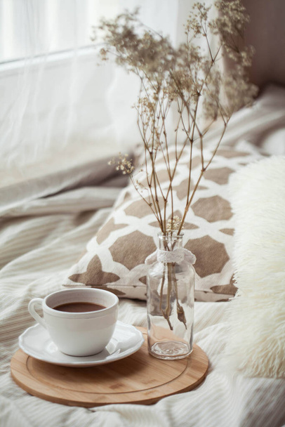 Egy csésze forró kakaó, egy faállvány, egy szárított virág egy üvegvázában az ágyon. Hajléktalanság. - Fotó, kép