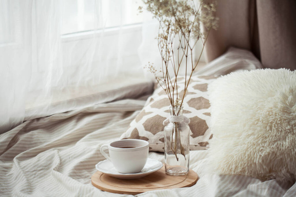 Šálek horkého kakaa, dřevěný stojan, sušená květina ve skleněné váze na posteli. Homeliness. - Fotografie, Obrázek