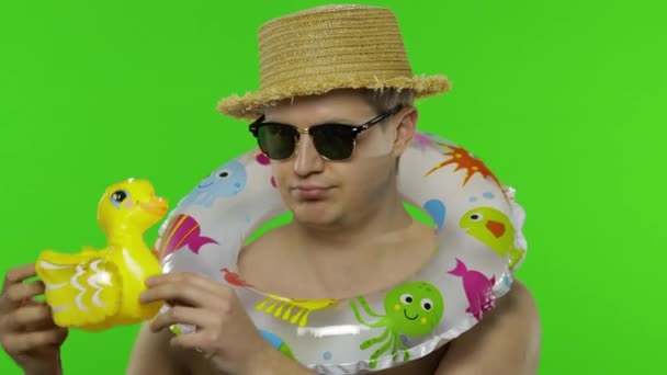Ing nélküli fiatalember turista úszás gyűrű vállán játszik kacsajáték - Felvétel, videó