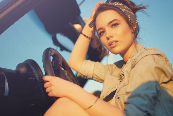 Young beautiful girl sitting in cabrio car on sunset wait for friends and think about perfect weekend - 写真・画像