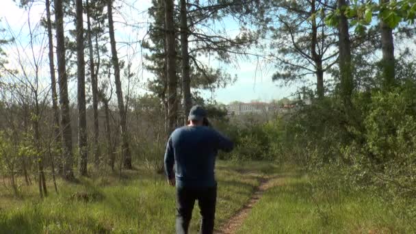 a man talking on a cell phone goes down a forest path. - Footage, Video