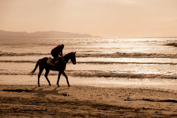 Ayia Eirini, Cyprus - 24 March, 2019: Man riding on a brown galloping horse on Ayia Erini beach in Cyprus against a rough sea - Foto, afbeelding