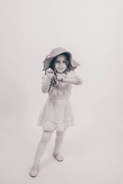Aranyos kislány ruhában. Kislány kalapban és ruhában a stúdióban.A gyermek érzelmei. - Fotó, kép