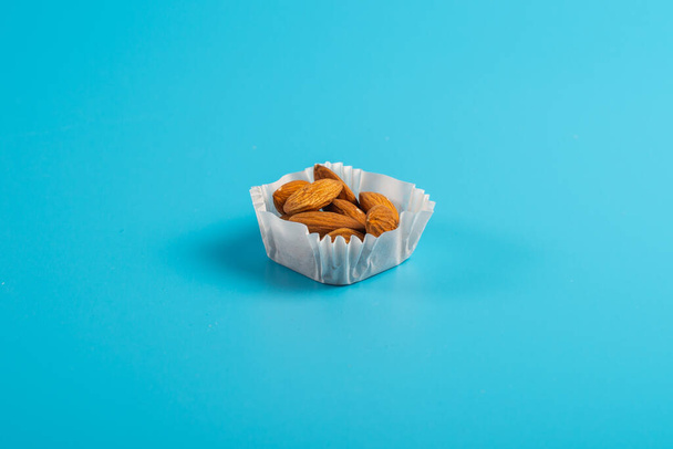 a portion of almonds in a paper cupcake mold on a blue background - Foto, Imagen