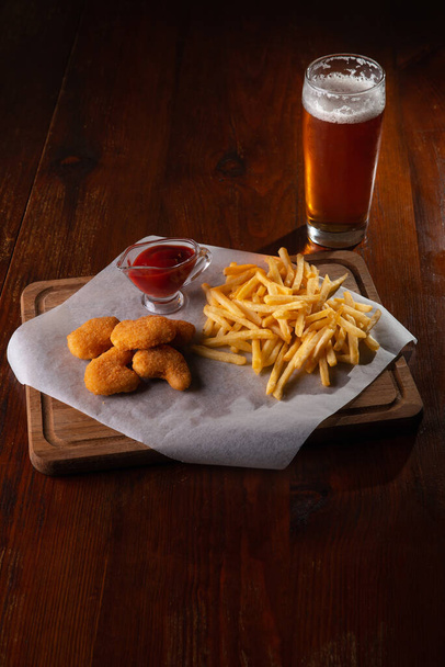 Nuggets french fries and sauce on a dark wooden background with beer - Foto, immagini