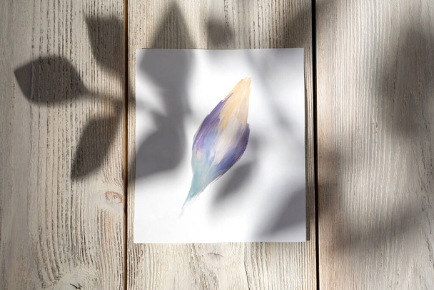 Purple painted abstract flower on a wooden background with the shadow of a branch with leaves. - Photo, Image