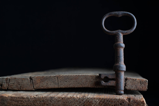 three old rusty keys stand on old wooden board against a dark background - Foto, Bild