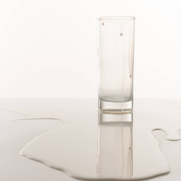 Empty glass stands among spilled milk on the table - Fotoğraf, Görsel