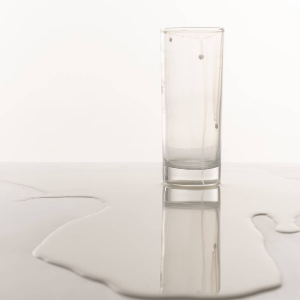Fehér tej kiömlött és fröccsent a fehér padló felületén és üres üveg - Fotó, kép