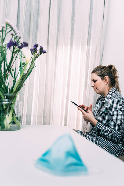 Koronavírus. Fénykép egy nőről, aki az okostelefonjával beszélget, arcmaszkkal az asztalon. Vírusmegelőzés és protokollok. Maradj otthon. Bezárás - Fotó, kép