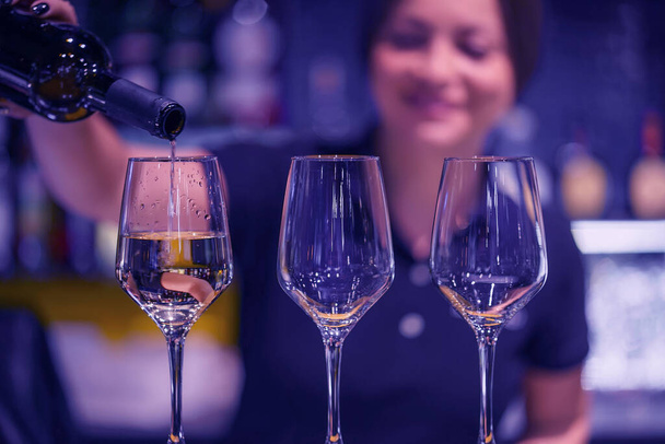 Femme barman souriante, verse du vin blanc dans un verre d'une bouteille. Temps de nuit
. - Photo, image